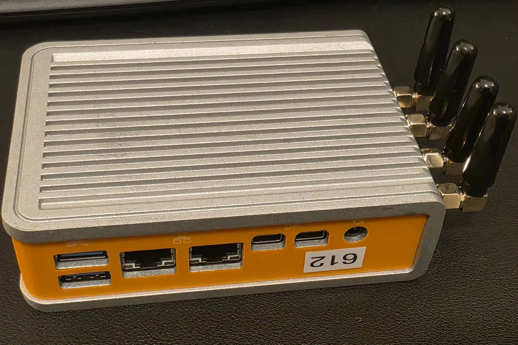 A fanless Logic Supply CL210G-P industrial mini-PC — one of the x86 router builds — in a ribbed silver aluminum case with an orange front bezel, four stubby antennas fanned to one side, and dual Ethernet plus USB ports.